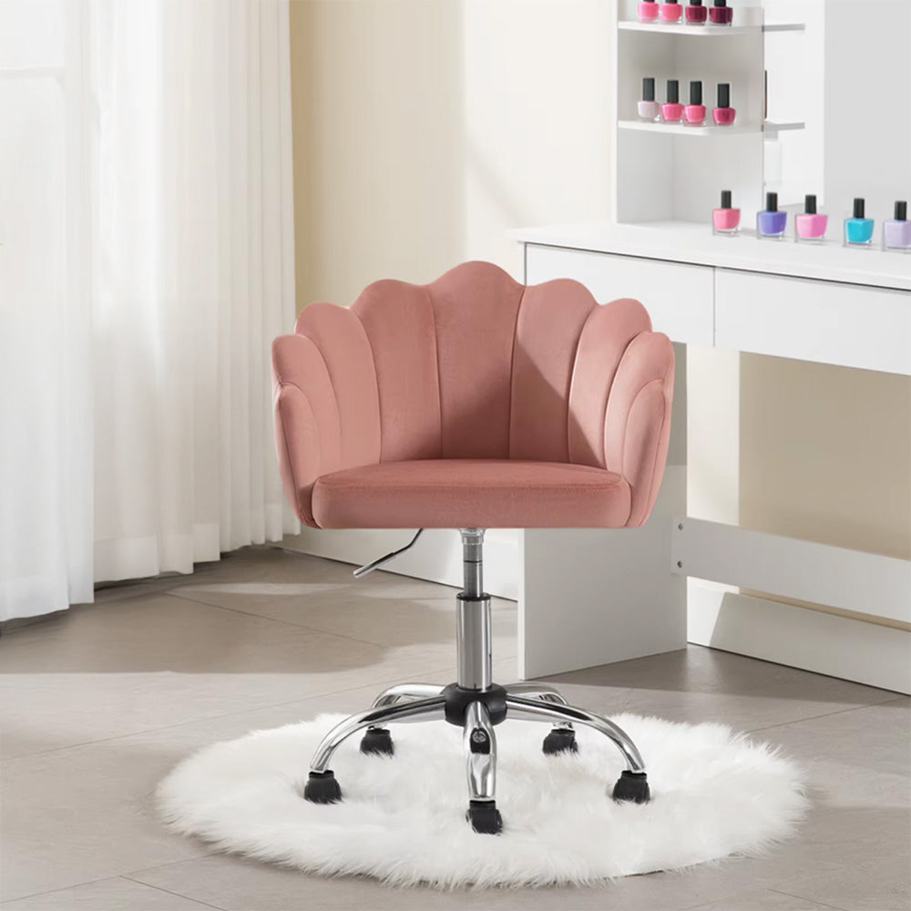 Chaise prothésiste ongulaire en velours rose placée sur un tapis blanc duveteux, devant une coiffeuse avec des vernis à ongles colorés.