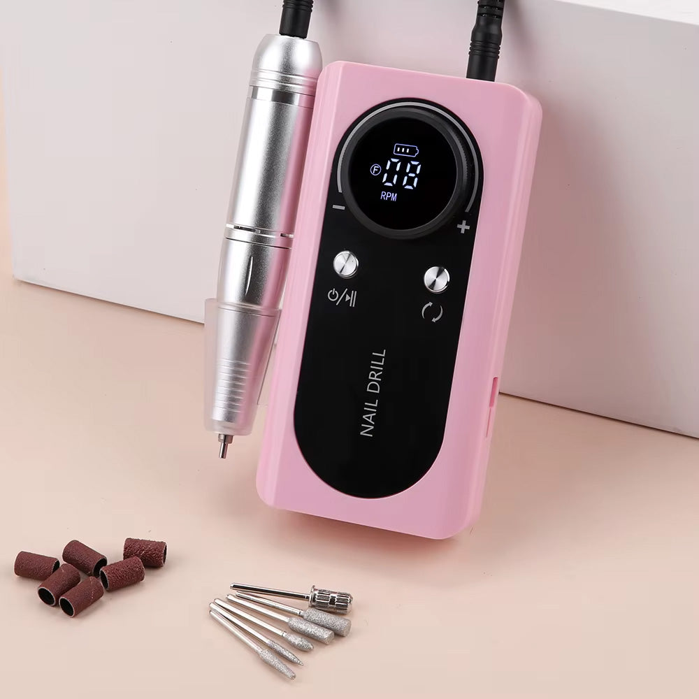 Vue rapprochée de la ponceuse à ongles rose avec ses embouts abrasifs et forets métalliques posés à côté, illustrant la précision et la qualité du kit.