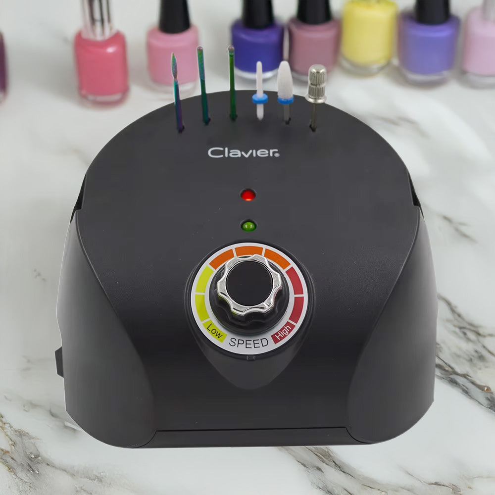 Gros plan sur la ponceuse noire en fonctionnement avec embouts insérés, posée sur une table avec plusieurs flacons de vernis colorés en fond.