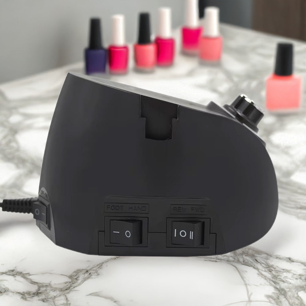 Vue arrière de la version noire de la ponceuse, montrant les interrupteurs pour le mode pied/main et le sens de rotation (avant/arrière), posée sur une surface en marbre avec des vernis en arrière-plan.