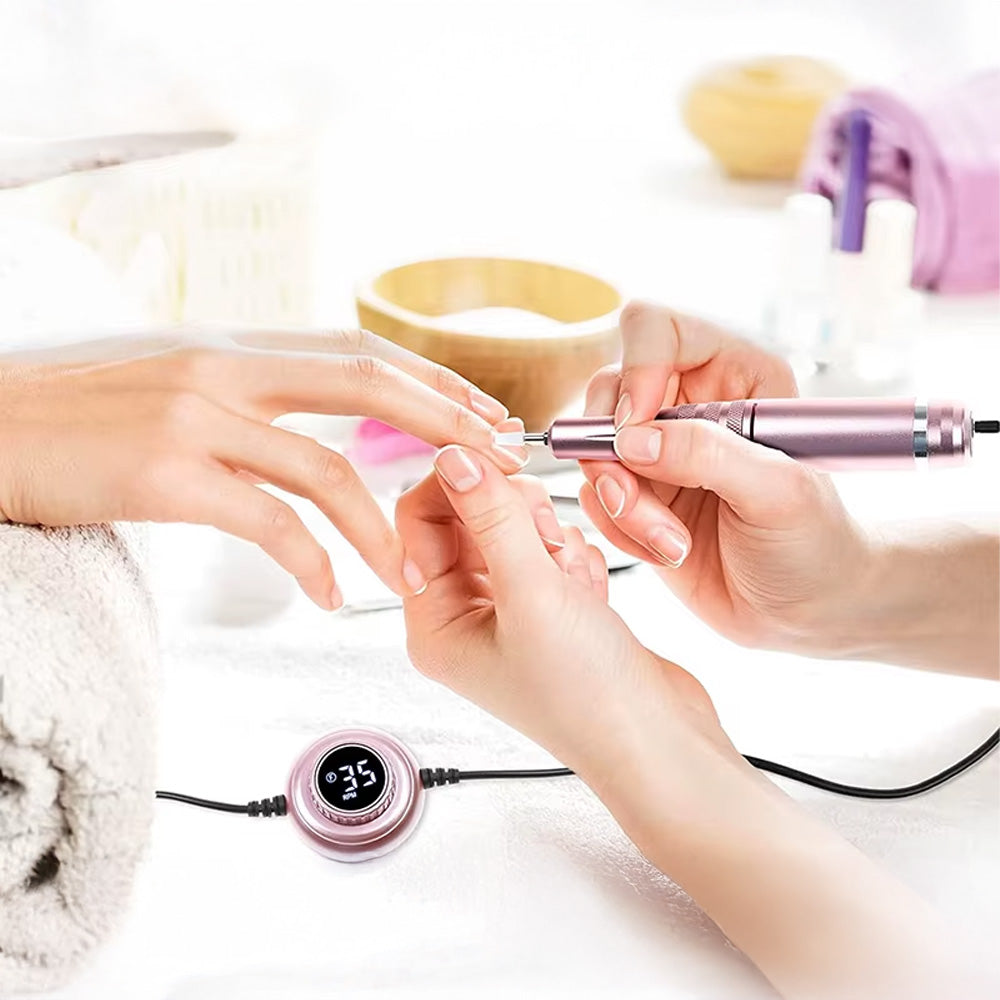 Séance de manucure avec la ponceuse à ongles électrique rose métallisé, utilisée pour le soin des cuticules. Le contrôleur LCD est visible en fonctionnement, indiquant la vitesse de rotation.