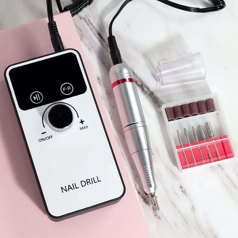 Ponceuse à ongles professionnelle 45000 RPM posée sur une surface en marbre rose, accompagnée de son coffret d’embouts et d’un capuchon de protection pour la pièce à main.