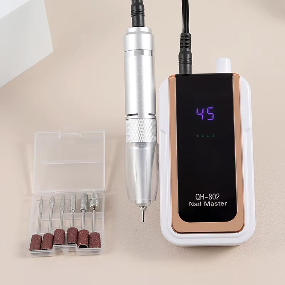 Ponceuse à ongles blanche et dorée 45000 tours/min posée sur une table avec sa boîte d'embouts de ponçage, idéale pour les professionnels de la manucure.