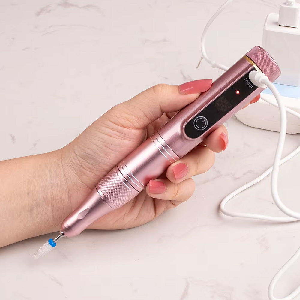 Une main tenant la ponceuse à ongles rose métallisé en cours de charge, connectée via un câble USB.